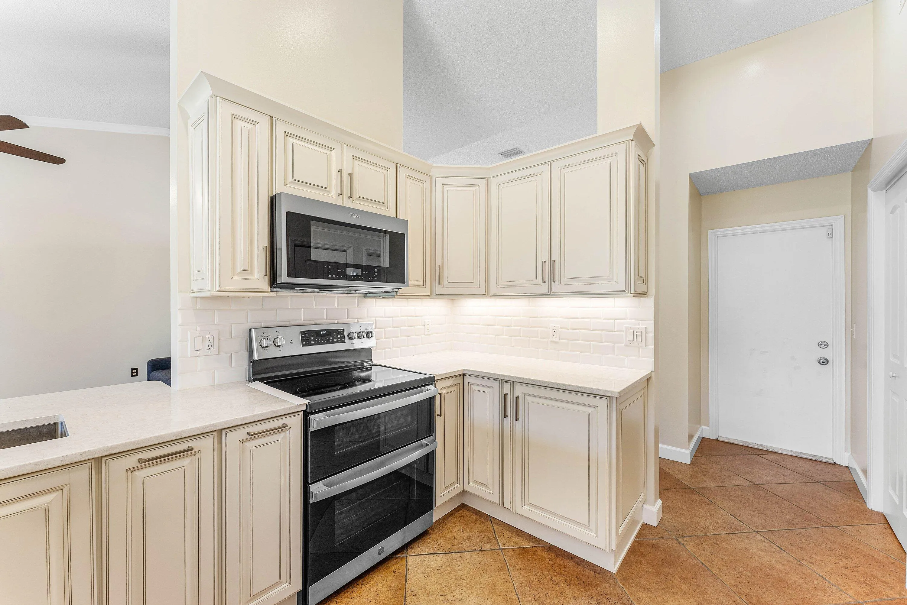 Kitchen featuring white cabinetry, a stainless steel microwave, a double oven range, white subway tile backsplash, and light-toned countertops