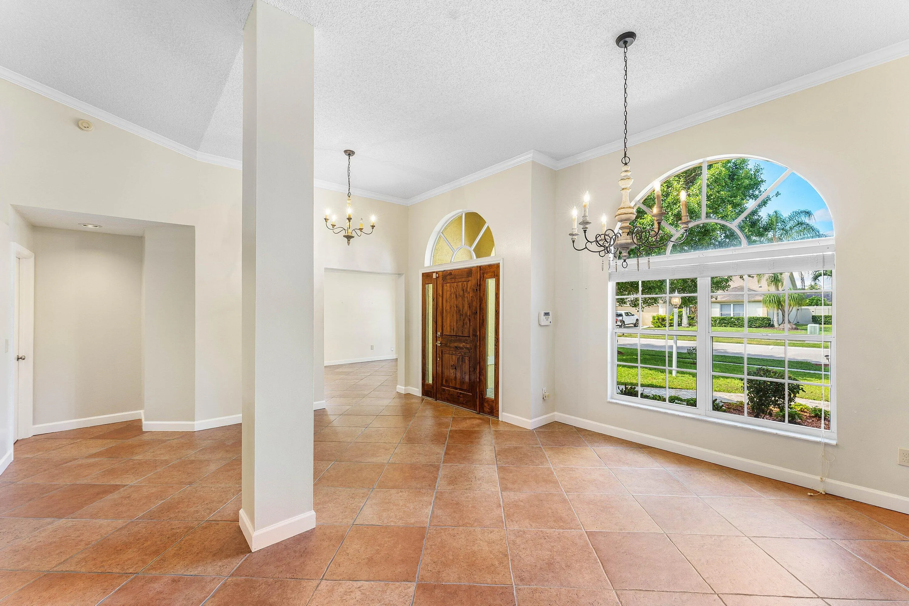 Vaulted ceilings, a dark wood-finish entry door with an arched transom, and an arched window with grid detailing