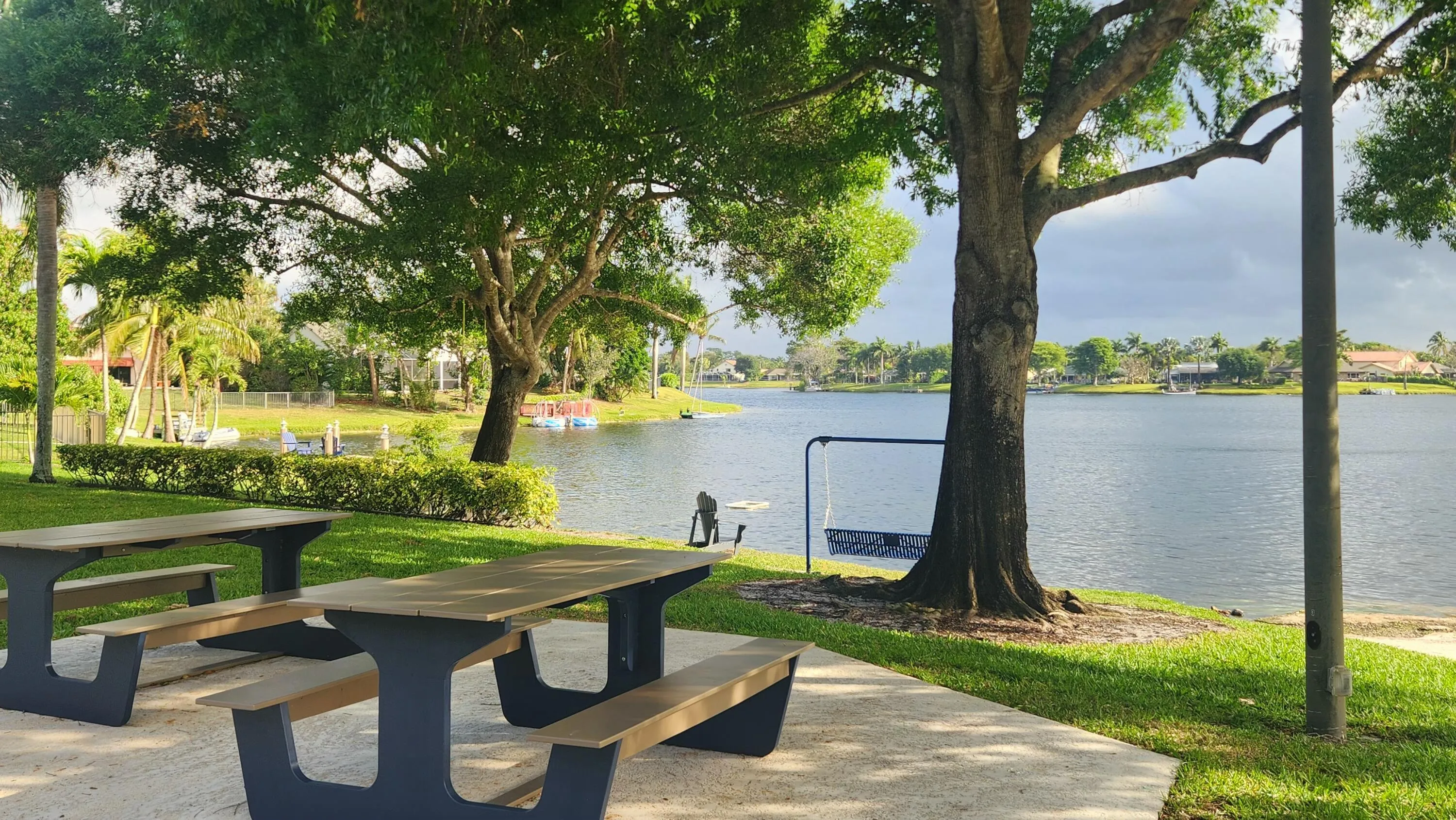 Expansive waterfront setting with mature trees, two permanent picnic tables, and a paved patio area
