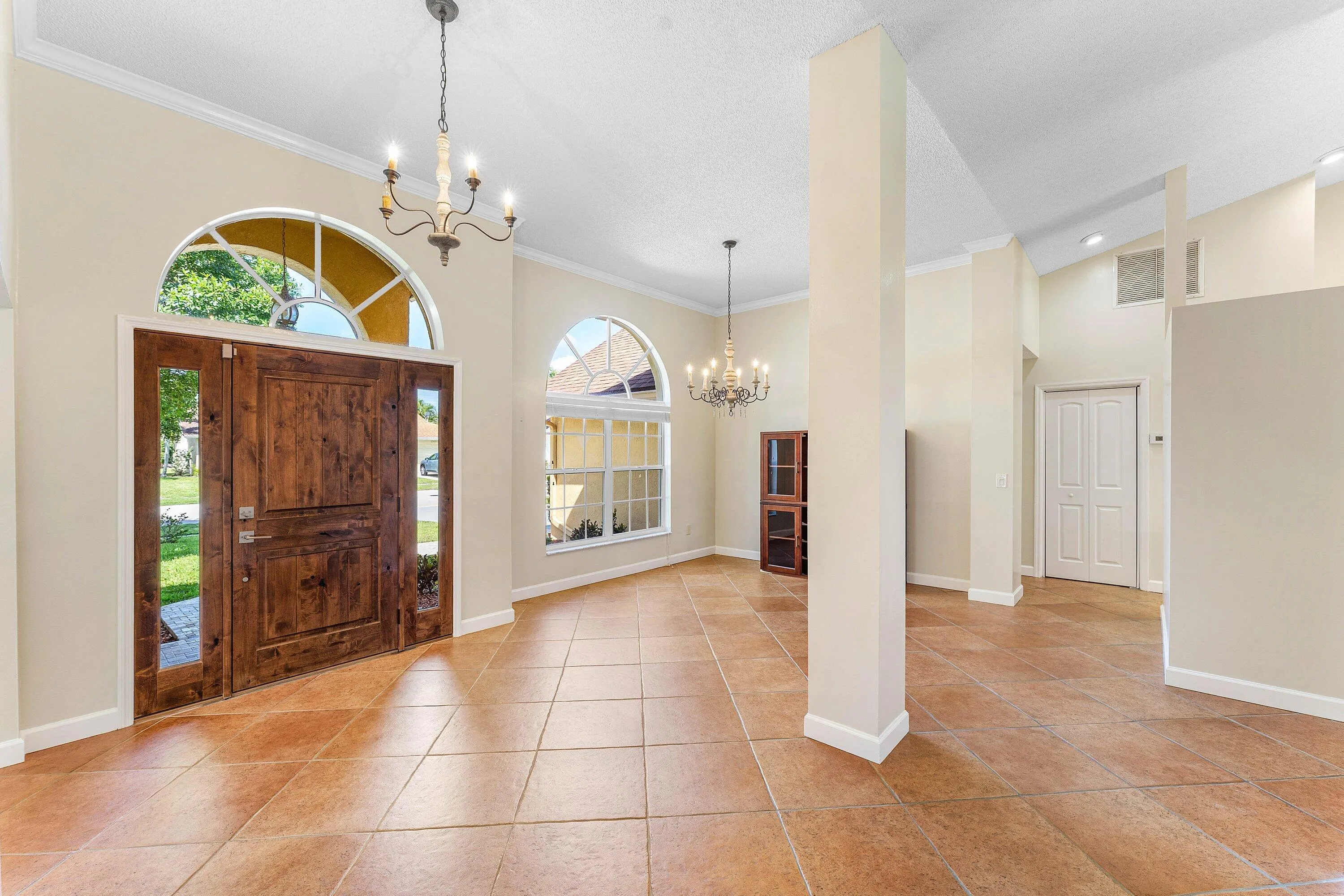 Vaulted ceilings, arched windows, tile flooring, wood-panel entry door, and decorative chandeliers