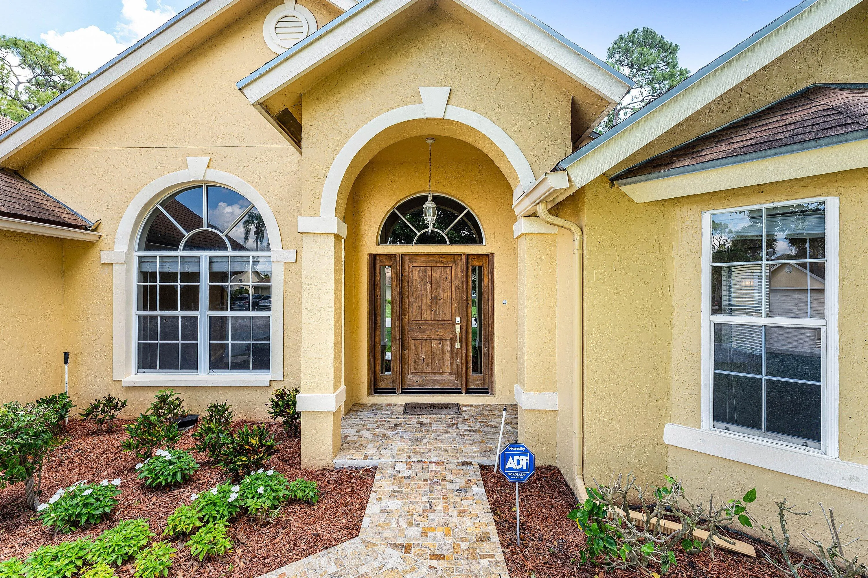 Stucco exterior with arched entryway, wood-paneled double entry doors, decorative transom window, and arched window with white framing