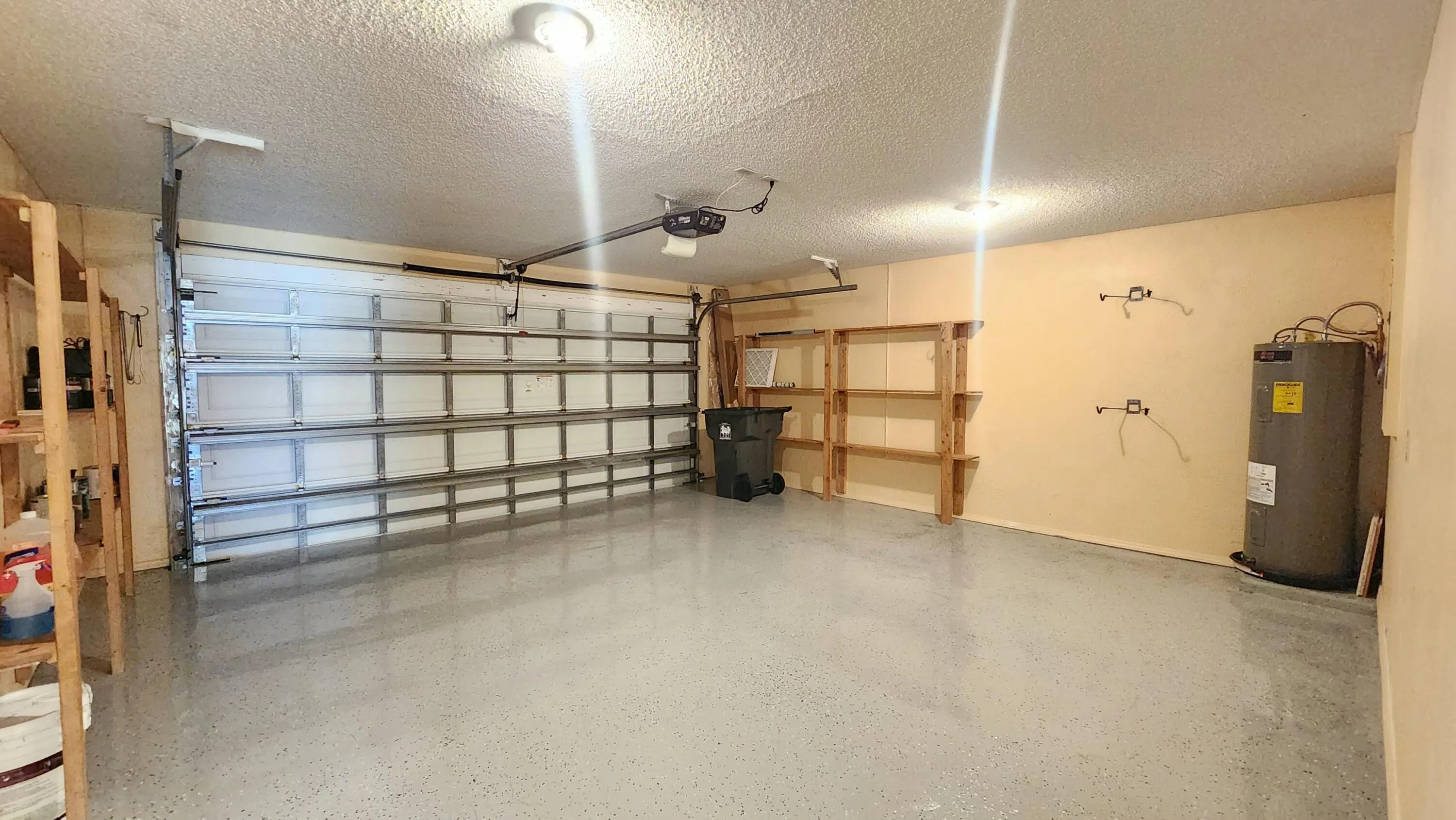 Spacious garage featuring a durable epoxy-coated floor, built-in shelving, and a water heater