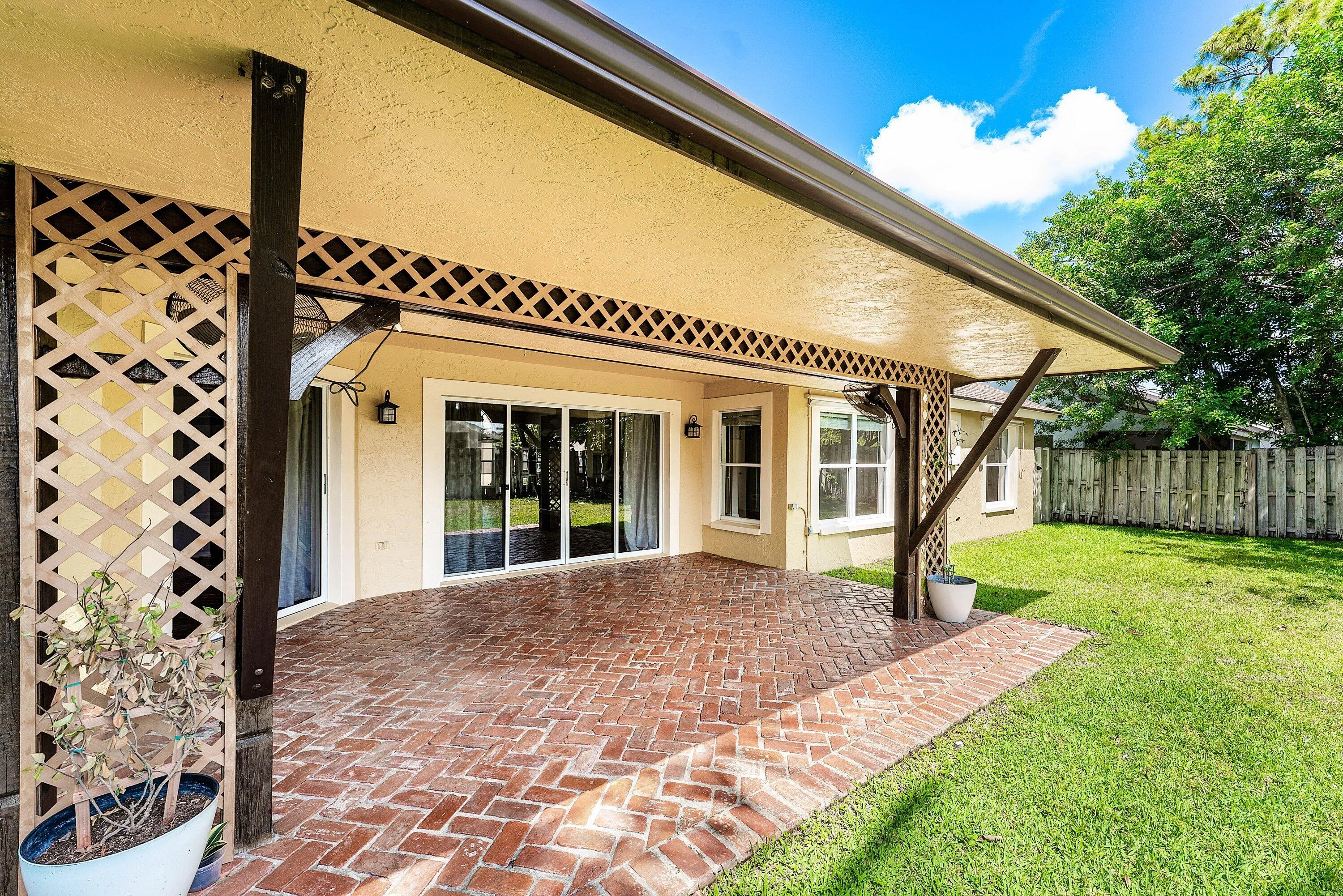 Covered patio featuring a herringbone brick-patterned surface, sliding glass doors, and decorative lattice accents