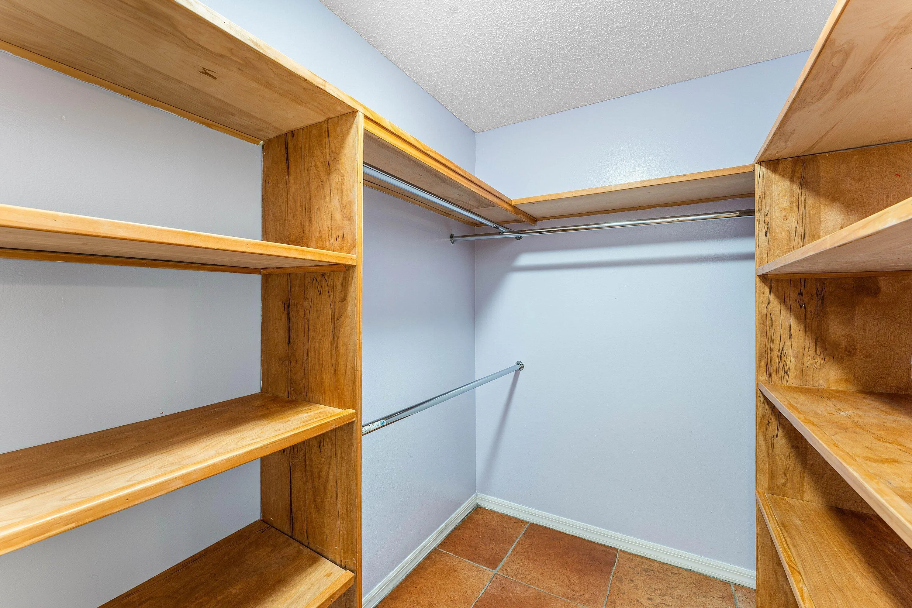Custom wood-finish shelving, built-in metal hanging rods, and terra cotta-style floor tiles