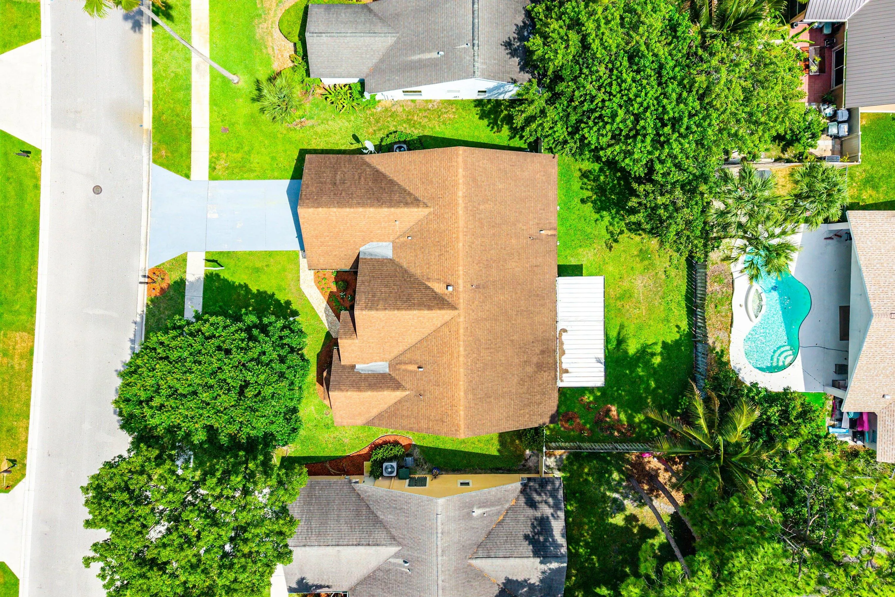 Asphalt shingle roof, well-maintained lawn, mature trees, concrete driveway, and backyard swimming pool