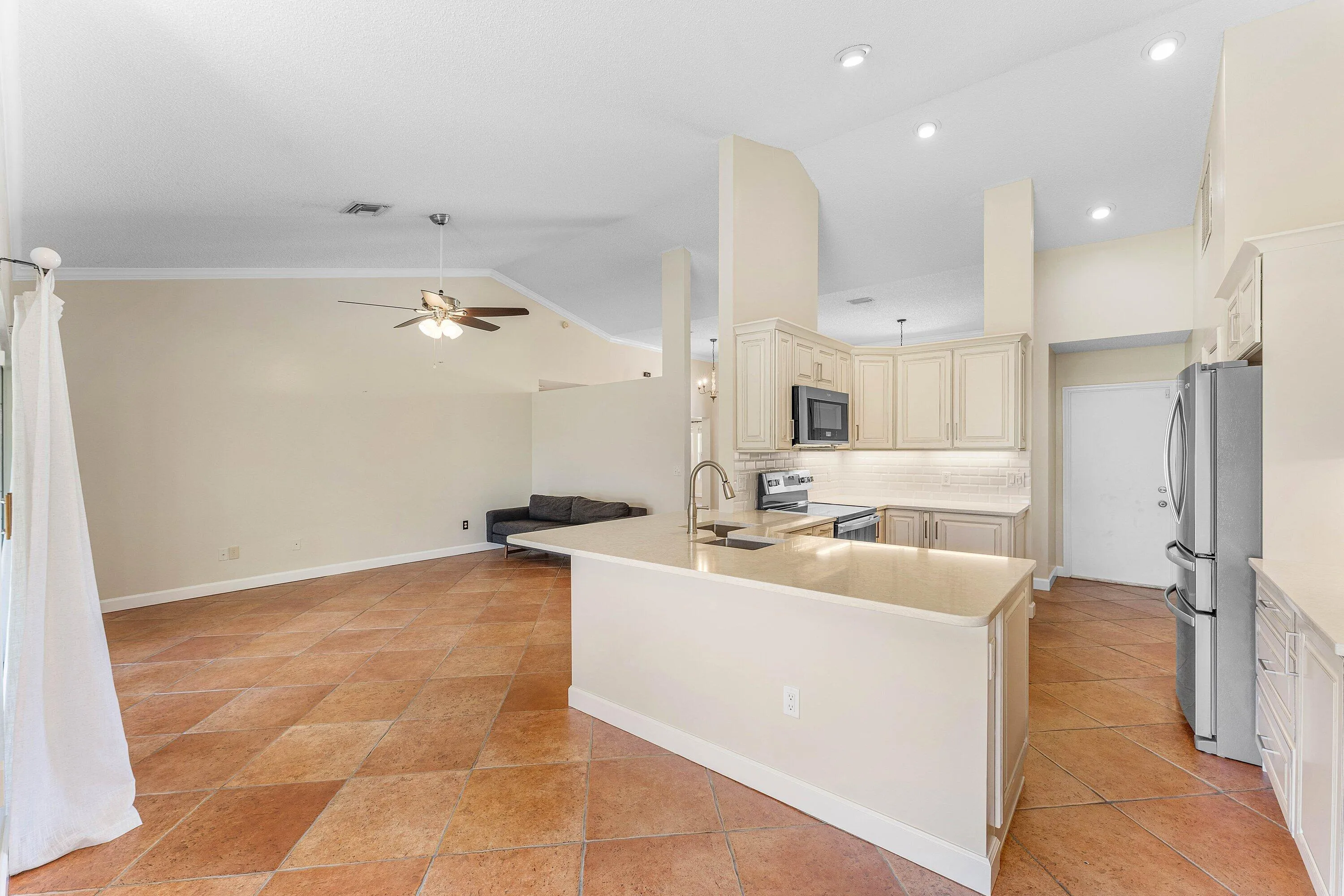 Open-concept design featuring vaulted ceilings, tile flooring, built-in kitchen cabinetry, and stainless steel appliances
