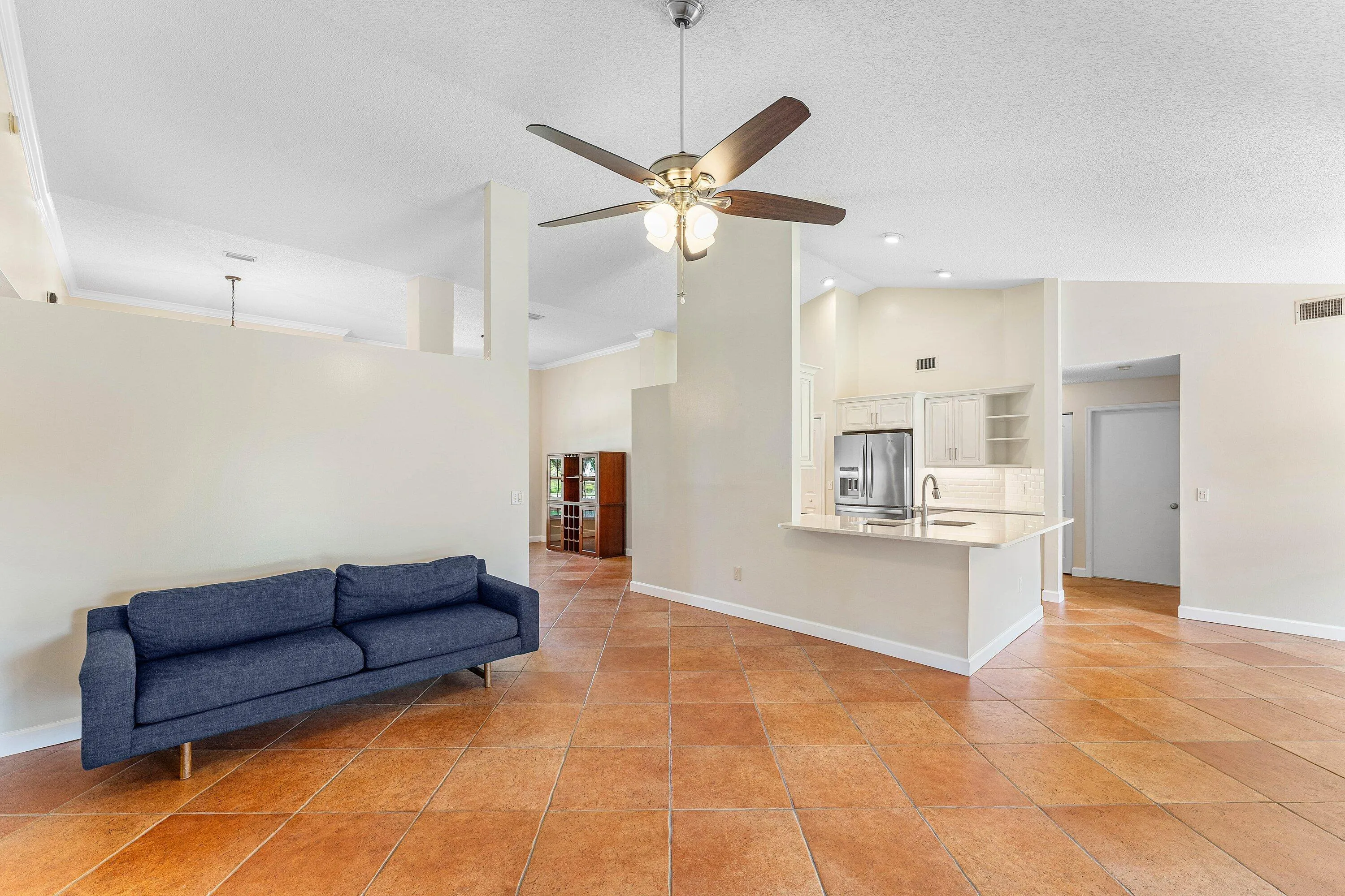 Spacious open-concept interior featuring vaulted ceilings, tile flooring, and a kitchen with stainless steel appliances and white cabinetry