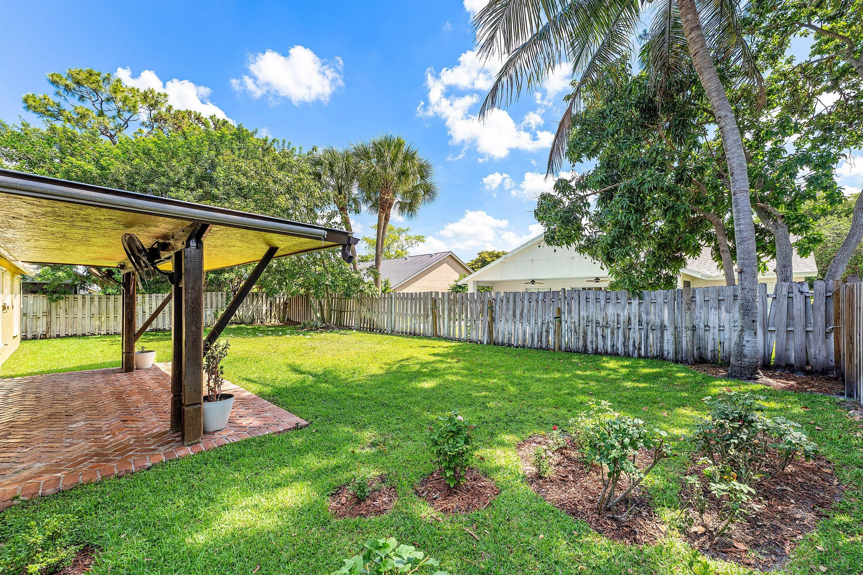 Expansive backyard featuring a brick paver patio, a covered structure with ceiling fan, a privacy fence, and trees