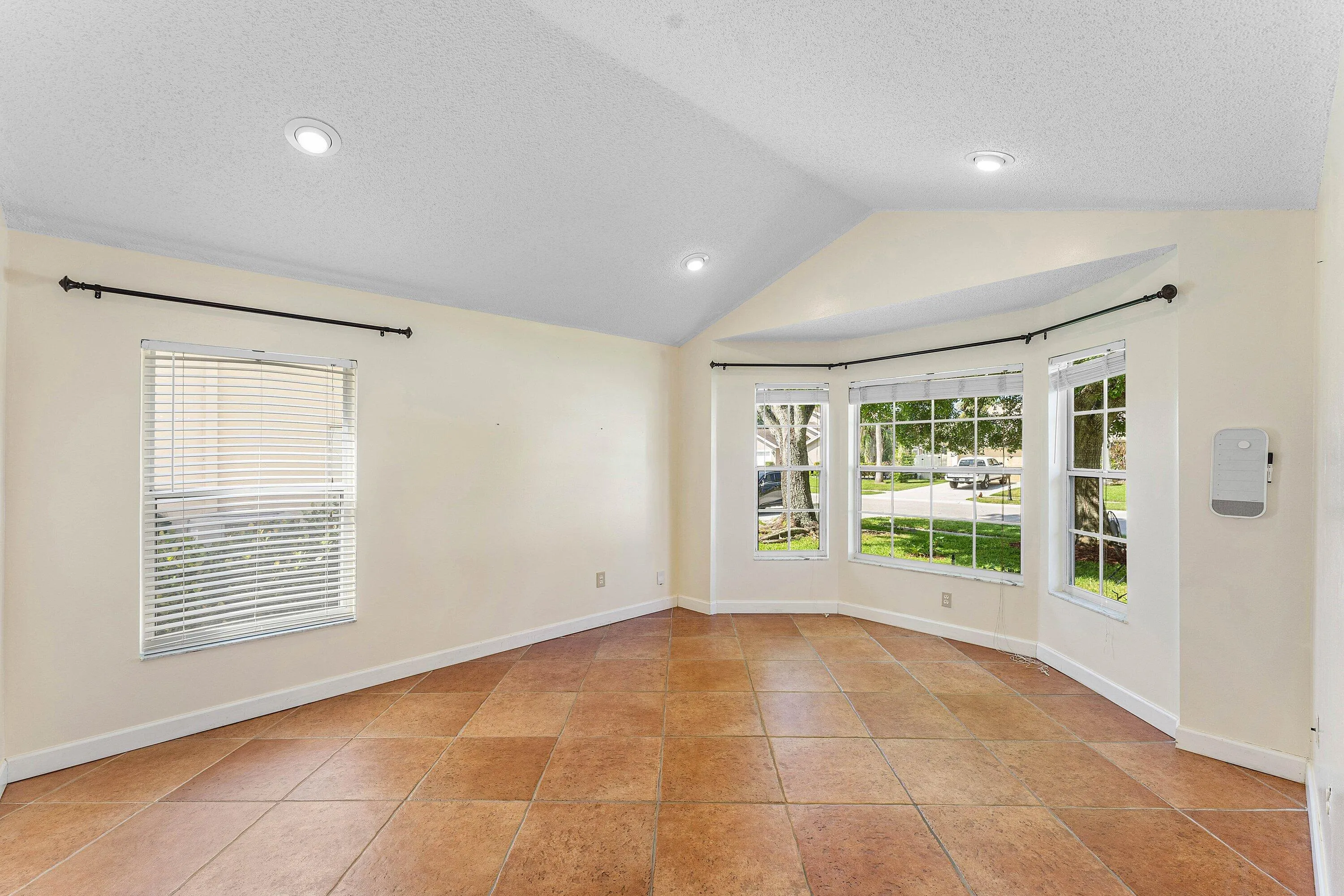 Vaulted ceiling with recessed lighting, bay windows, tile flooring, and neutral wall tones