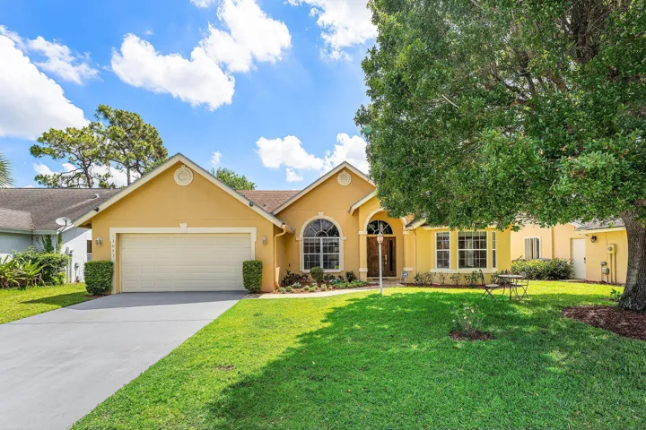 Single-story residence featuring attached two-car garage, arched entryways, and a mature front yard tree