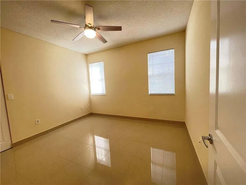 Ceiling fan with integrated lighting, two windows with blinds, polished tile flooring, and a neutral color palette