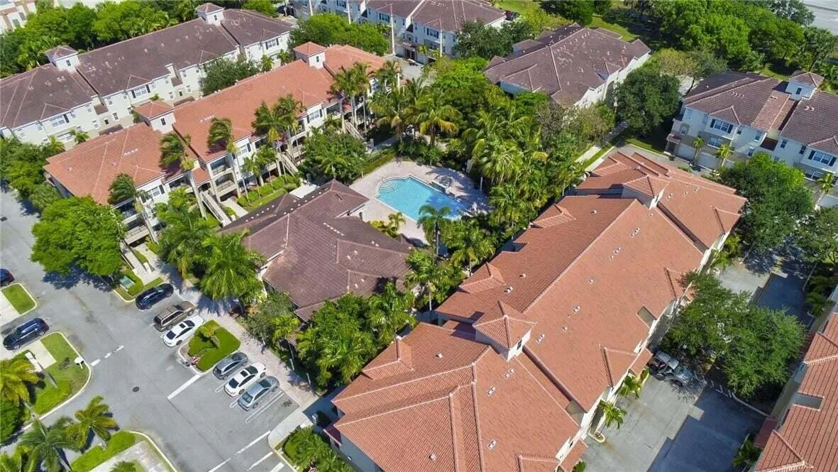 Terracotta tile roofing, multi-story residences, mature tropical landscaping, community swimming pool, and dedicated parking areas