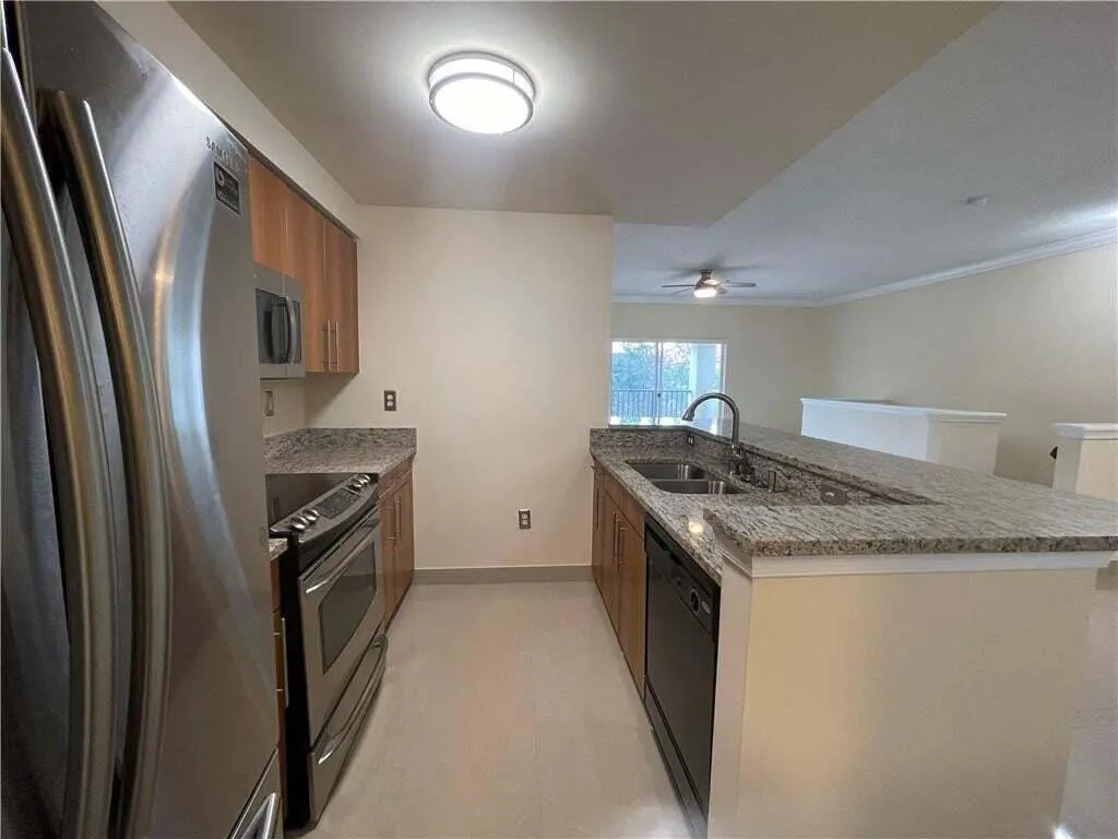 Kitchen featuring stainless steel appliances, wood cabinetry, granite countertops, an integrated kitchen island with sink, and tile flooring