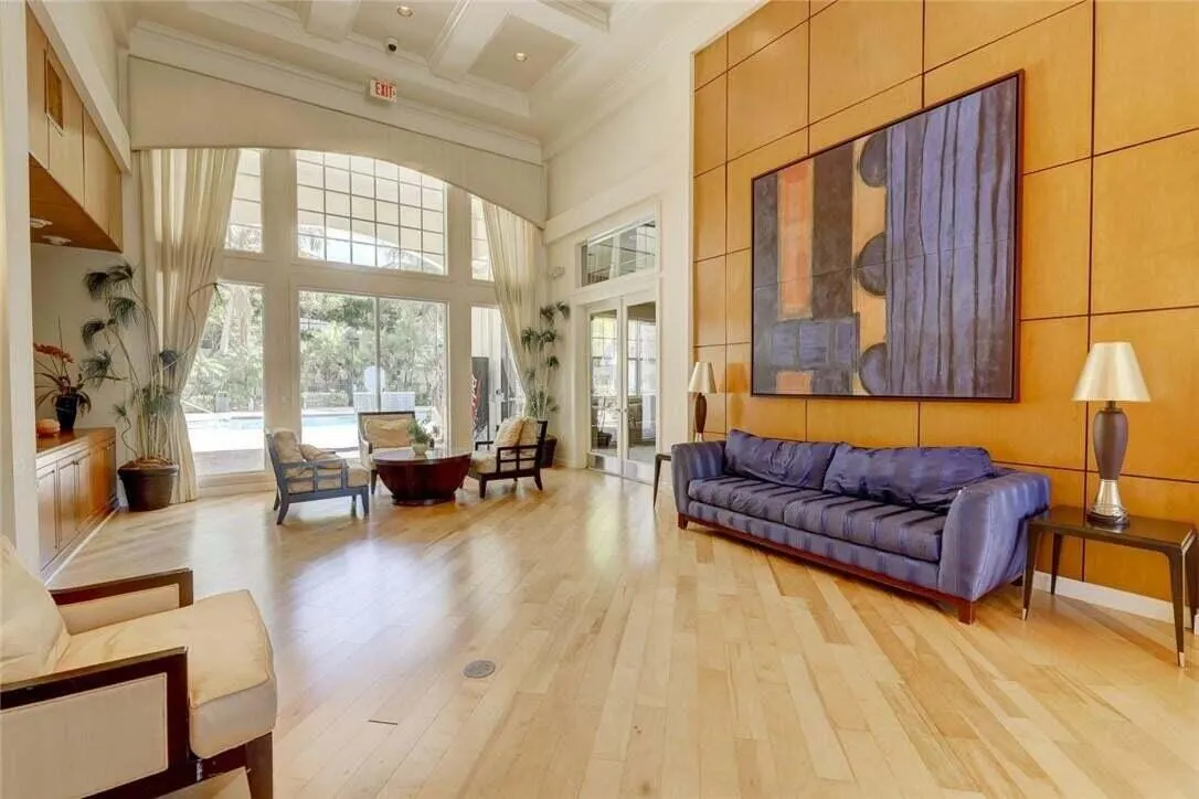 Expansive windows with arched transoms, wood-finish flooring, coffered ceiling, wood-paneled accent wall, and built-in cabinetry