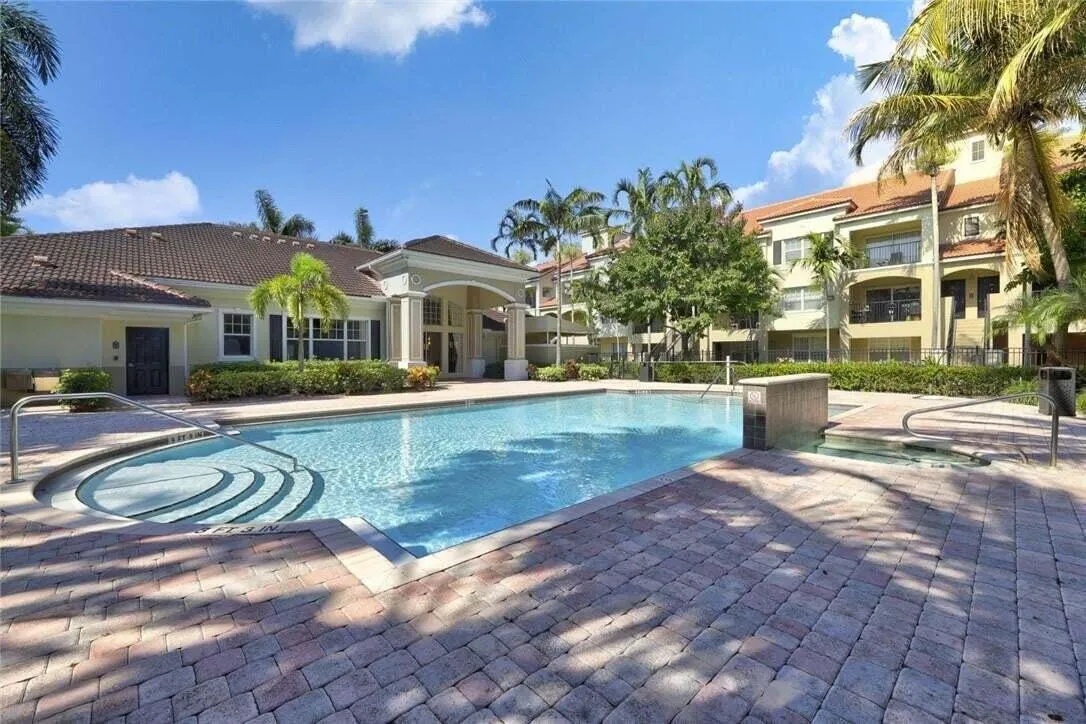 Community swimming pool with integrated steps, surrounded by paver patio and tropical landscaping