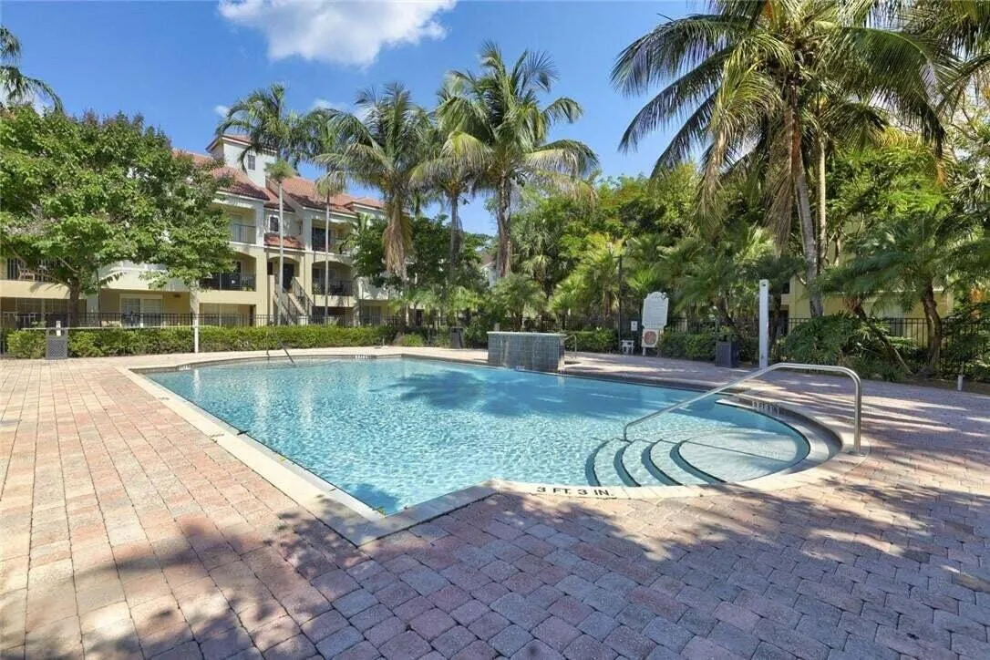 Resort-style pool with integrated steps and handrail, surrounded by brick paver decking and mature palm trees