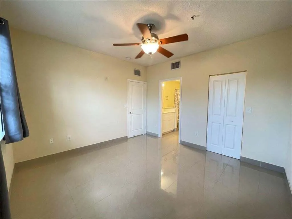 Spacious room with tile flooring, ceiling fan with light fixture, and two panel doors