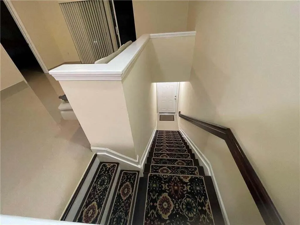 Staircase with wood-finish treads and patterned runners, featuring a dark wood-finish handrail and light-toned walls
