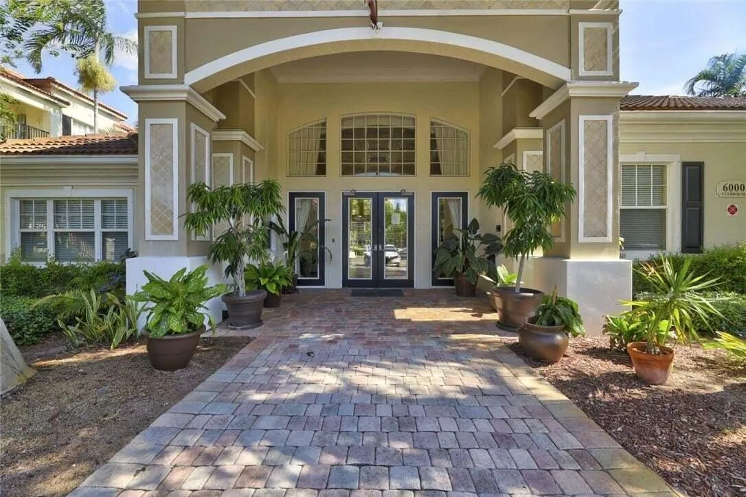 Stucco exterior with an arched entryway, decorative columns, transom windows, double glass entry doors, and a paver walkway