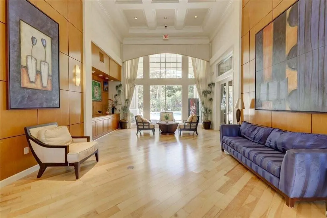 Hardwood flooring extending through a spacious room featuring high coffered ceilings, extensive wood paneling, built-in cabinetry, and large arched windows with transoms