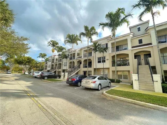 Multi-story building featuring stucco exterior, multiple balconies with black railings, and mature palm trees