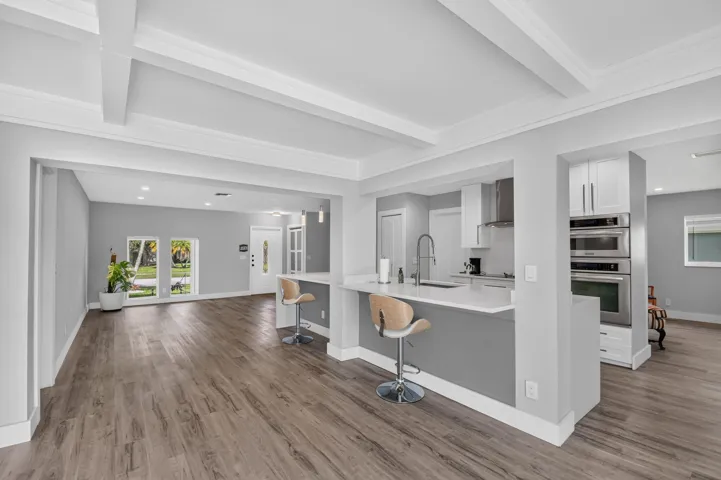 Kitchen island with stone countertop, stainless steel appliances, wood-finish flooring, recessed lighting, and exposed ceiling beams
