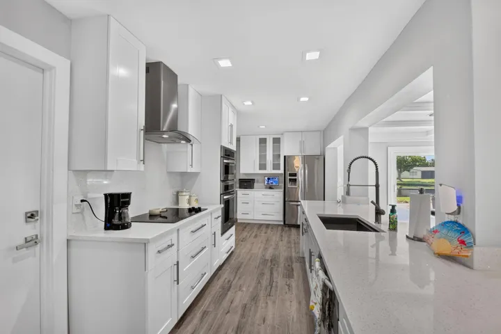 White shaker cabinetry, stainless steel appliances, wood-finish flooring, recessed lighting, and light-toned countertops