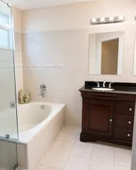 Enclosed soaking tub with wall-mounted fixtures, glass shower enclosure, wood-finish vanity with an undermount sink, dark countertop, and tiled flooring