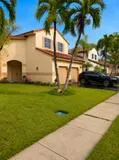 Stucco exterior with a tile roof, mature palm trees, an attached two-car garage, and a concrete sidewalk
