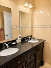 Dual oval undermount sinks with chrome-finish faucets, dark wood-finish vanity with cabinet storage, and a dark countertop