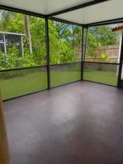 Screened enclosure with a solid roof, concrete flooring, and surrounding foliage