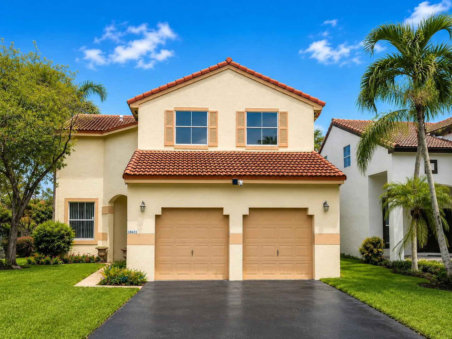 Stucco exterior with a tile roof, dual garage doors, decorative shutters, and mature landscaping
