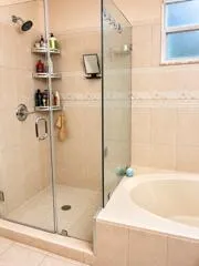 Glass-enclosed shower with a rainfall showerhead, a built-in corner shelving unit, and a tiled shower surround