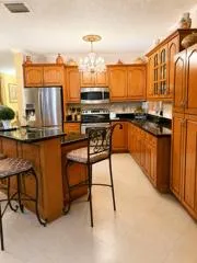 Wood-finish cabinetry with glass-front accents, dark countertops, stainless steel appliances, and a central island with bar seating