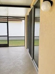 Screened patio with textured flooring, multiple sliding glass doors, and an exterior wall light fixture