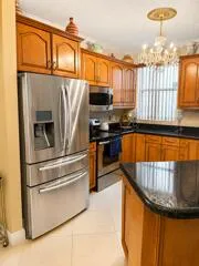 Stainless steel French door refrigerator, wood cabinetry, dark countertops, built-in stainless steel microwave, and tile flooring