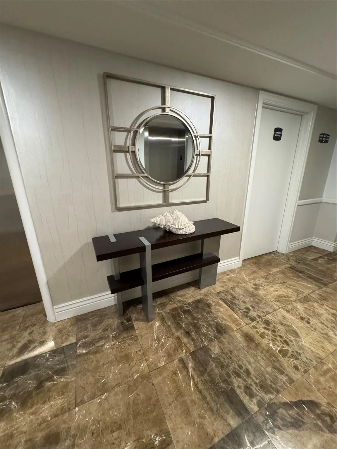 Marbled tile flooring, textured wall covering, decorative wall mirror, and a wood-finish console table