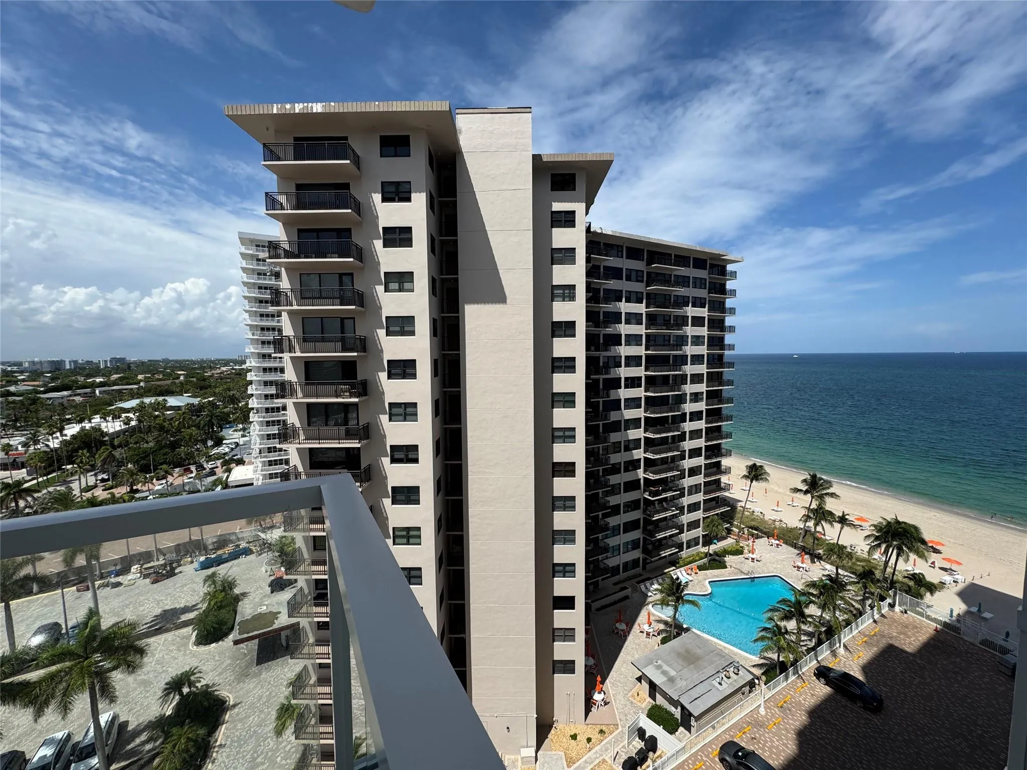 Modern high-rise building featuring multiple balconies, a ground-level swimming pool, and direct beach access