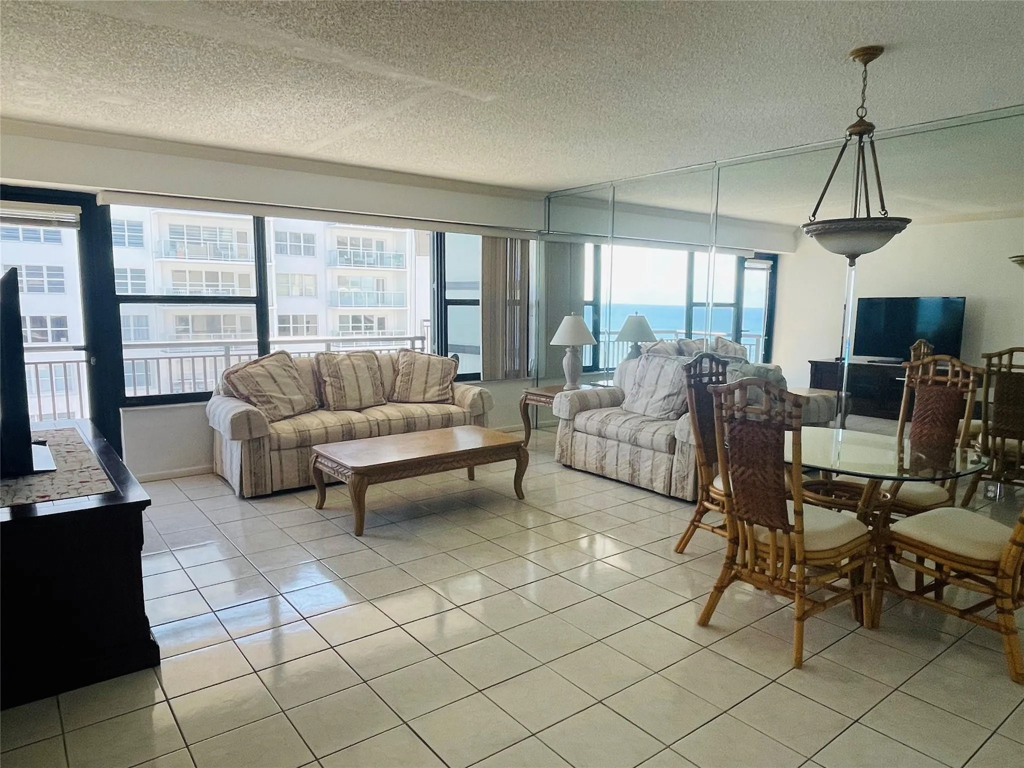 Tiled flooring throughout, wall of windows, glass panel balcony door, integrated wall mirror, and a ceiling-mounted light fixture