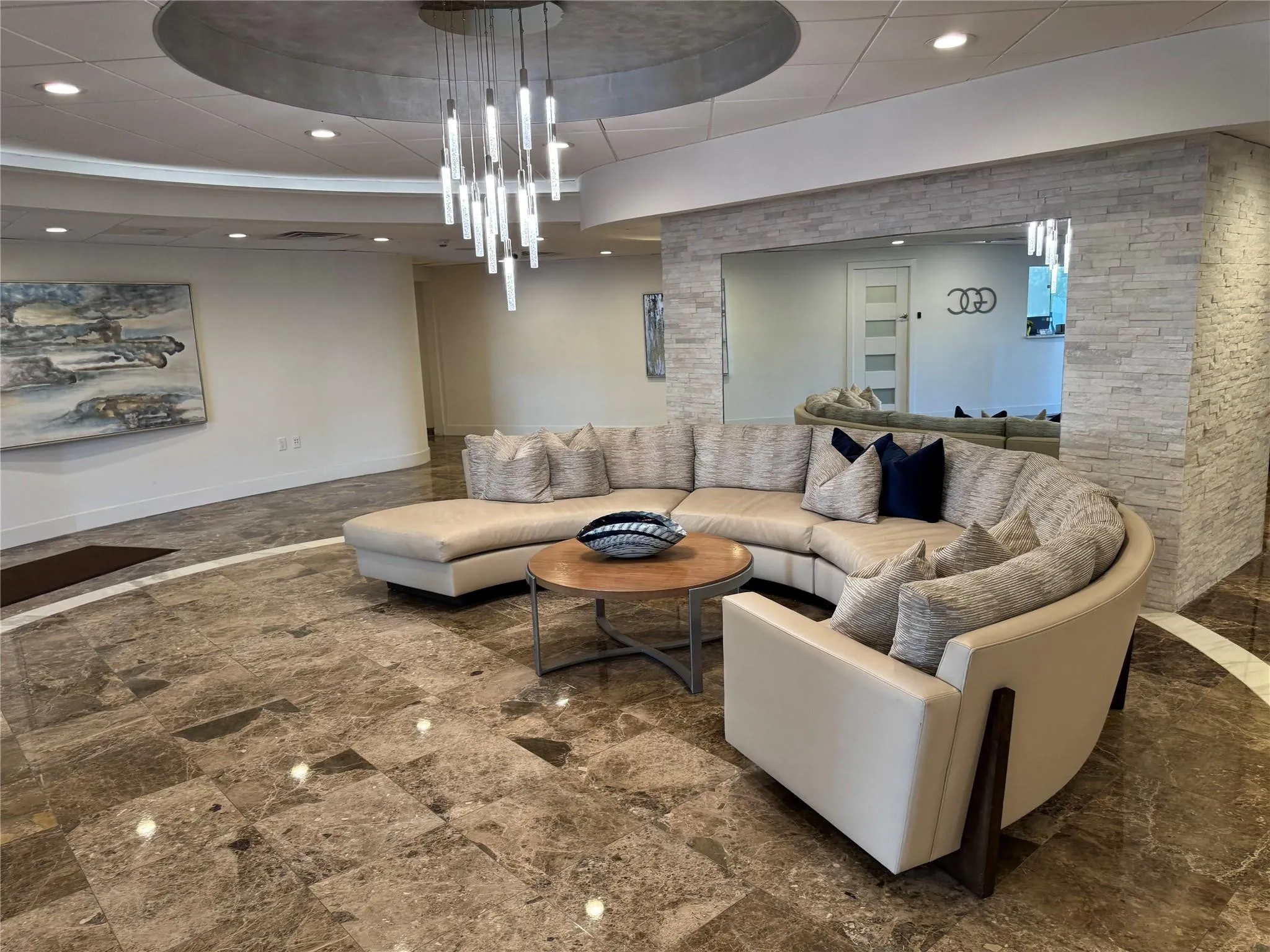 Polished stone flooring with contrasting inlay, elegant chandelier, recessed lighting, and stacked stone wall accents