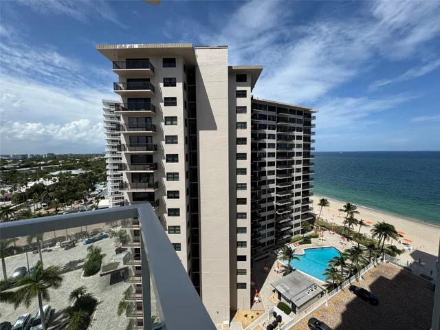 Modern high-rise building featuring multiple balconies, a ground-level swimming pool, and direct beach access