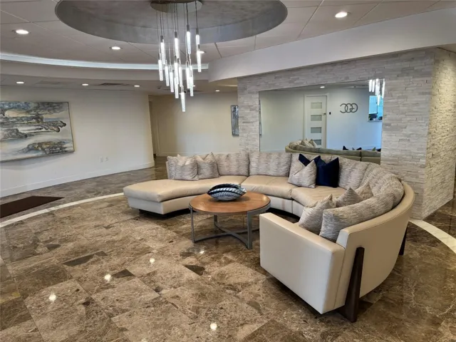 Polished stone flooring with contrasting inlay, elegant chandelier, recessed lighting, and stacked stone wall accents