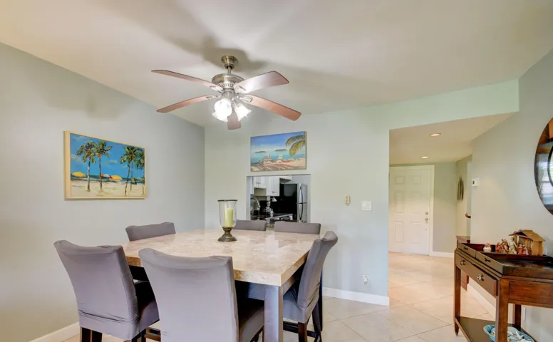 Dining area featuring a ceiling fan with integrated lighting, a rectangular dining table with a light-toned surface, and a pass-through opening to an additional room