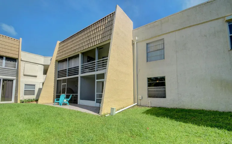Modern architectural home featuring a geometric facade with warm-toned exterior cladding, expansive glass sliding doors opening to the rear elevation, manicured lawn, and clean-lined contemporary design with mixed material finishes including concrete and wood-tone accents