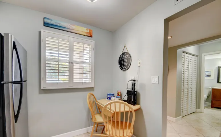 Stainless steel refrigerator, white plantation shutters, built-in wall-mounted table, louvered bi-fold closet doors, and recessed lighting