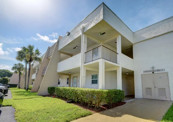 Multi-level building with stucco exterior, multiple balconies, and mature palm trees