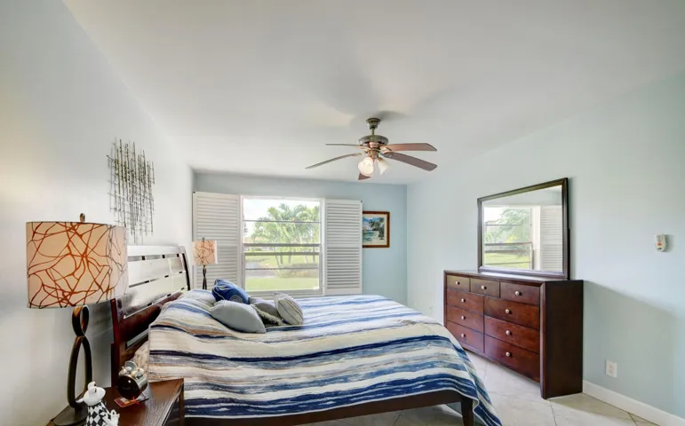 Spacious room with a ceiling fan, tiled flooring, and a large window featuring louvered shutters