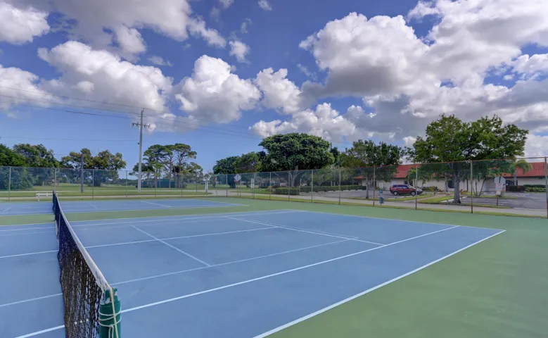 Two tennis courts featuring blue playing surfaces and green out-of-bounds areas