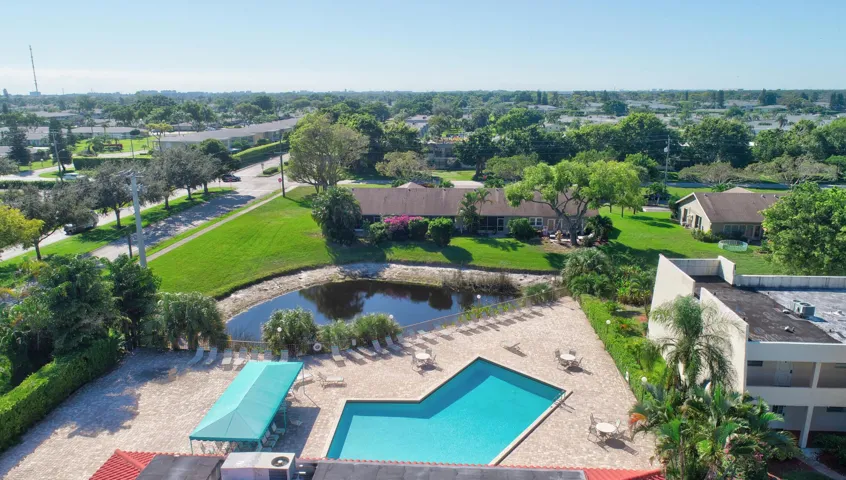 Community pool with an integrated spa, expansive paver deck, and surrounding lush landscaping
