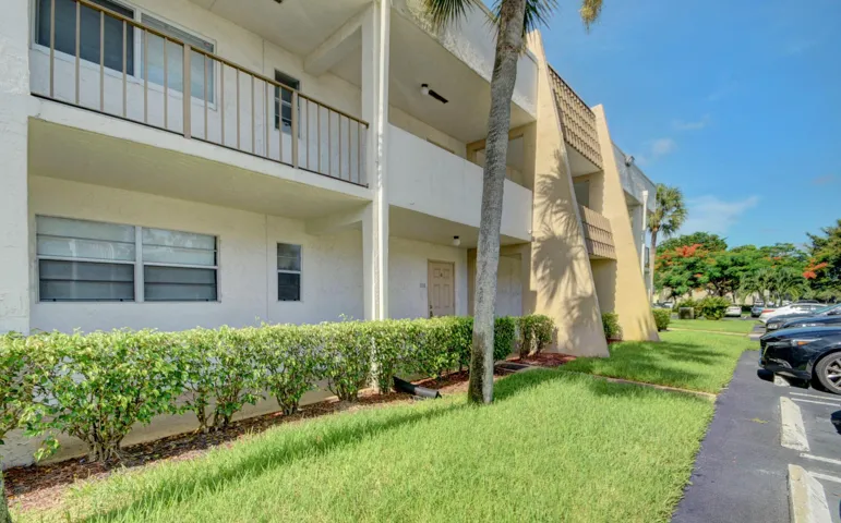 Multi-level stucco exterior, mature palm trees, manicured hedges, and assigned parking